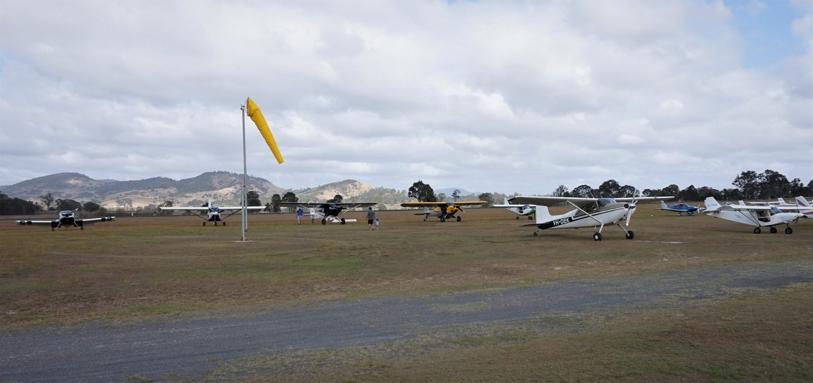 Aircraft parked on the grass at Gympie Aerodrome with the windsock and hills behind