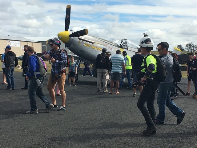 Visitors and a pilot walking past a warbird on the apron at YGYM